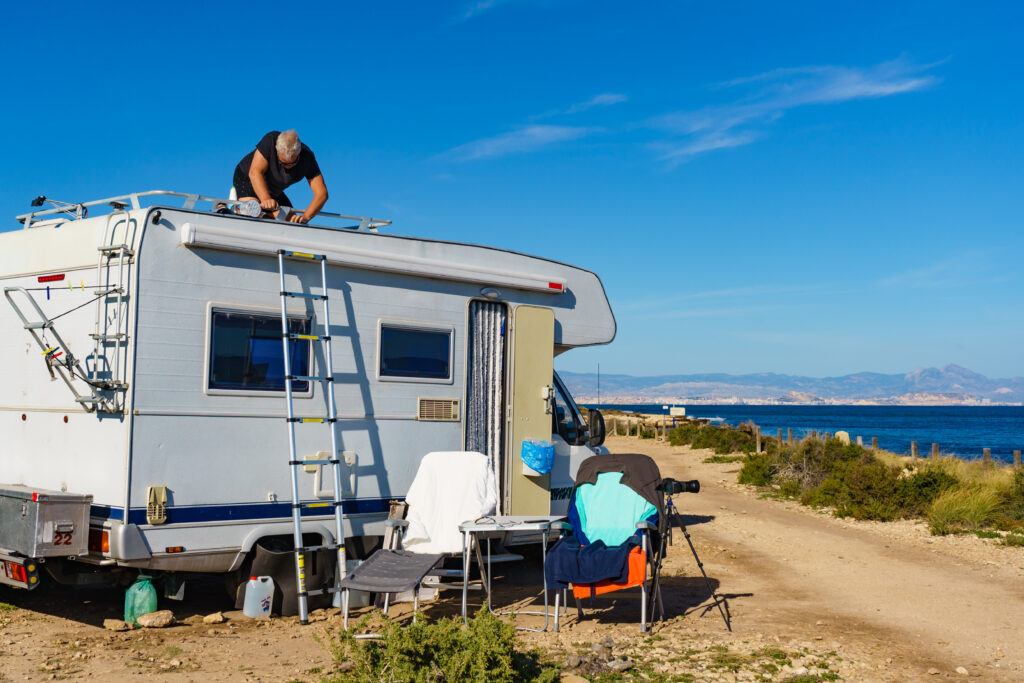 a man on top of a camper performing essential RV maintenance with a ladder leaning on the side of the camper